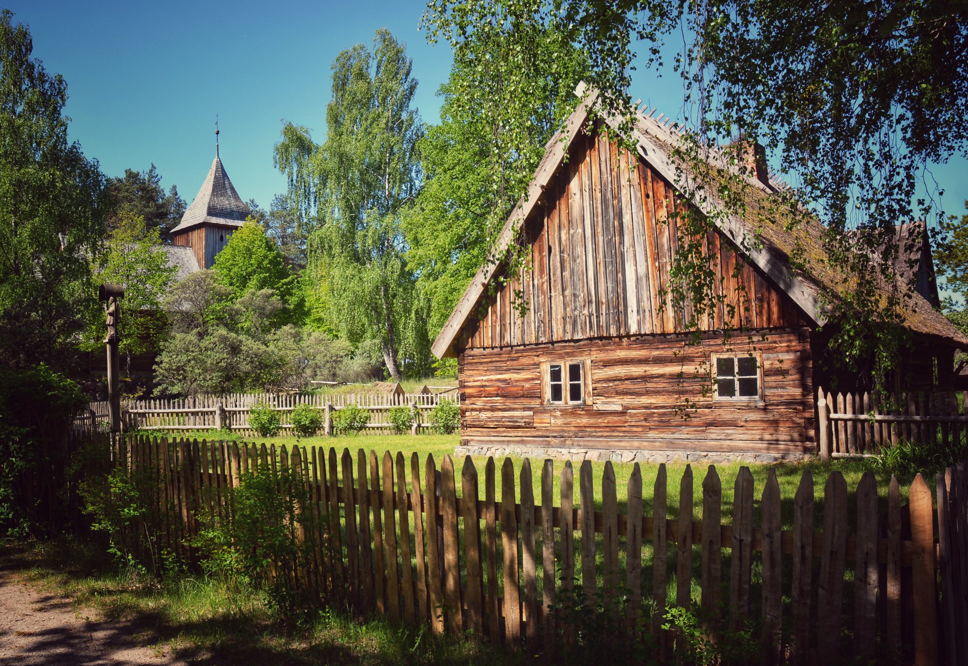 Widok na zabudowę skansenu we Wdzydzach Kiszewskich, Na pierwszym planie drewniana chata, w tle - kościół